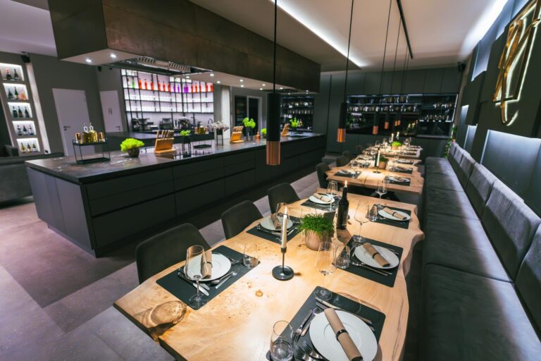 hochzeit & kleine hochzeitsfeier paderborn — kochkurs eventlocation 6 Lange eingedeckte Holztafel im dunklen Kochstudio – Hochzeitsdinner bei K wie Kochkunst Paderborn